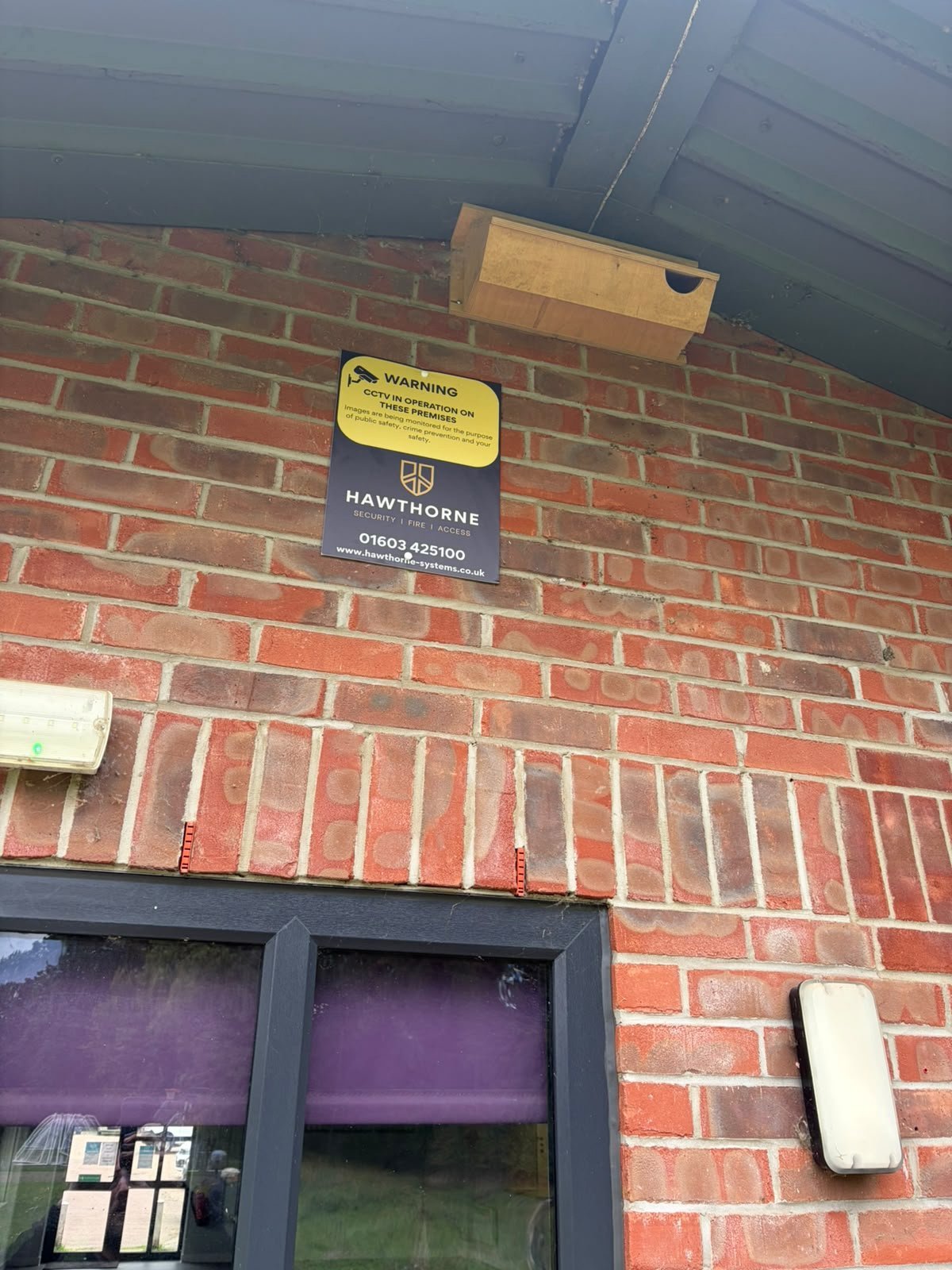 Hawthorne CCTV warning sign mounted high on a brick gable beneath the eaves of a council building.