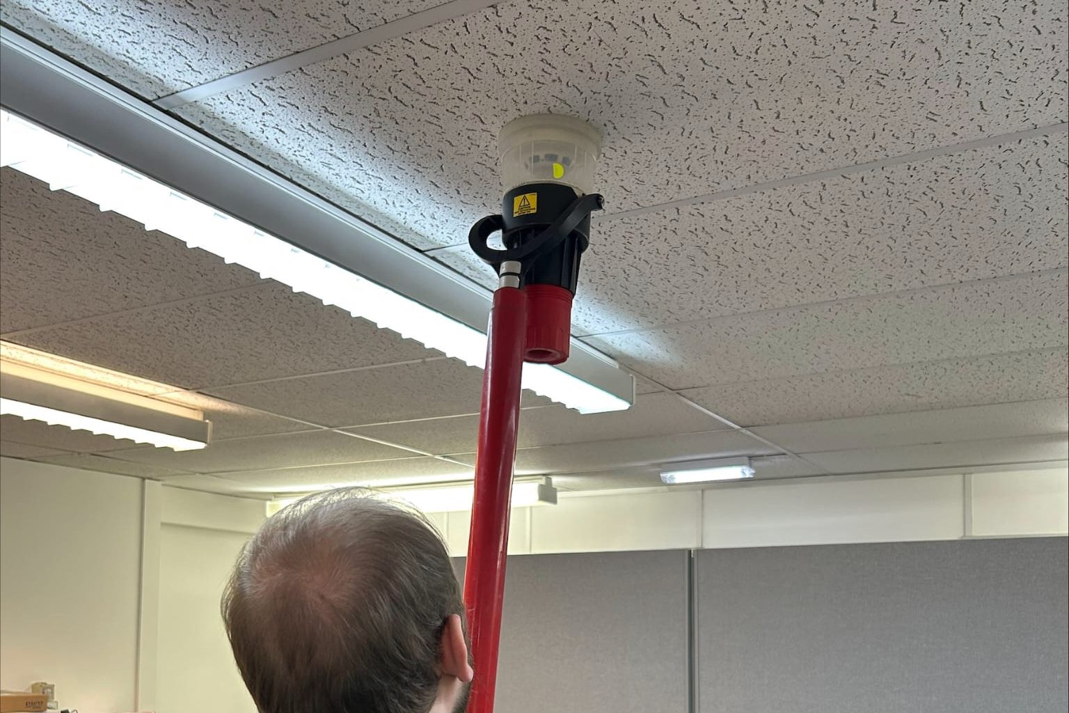 Engineer functionally testing a ceiling smoke detector with a detector test pole.