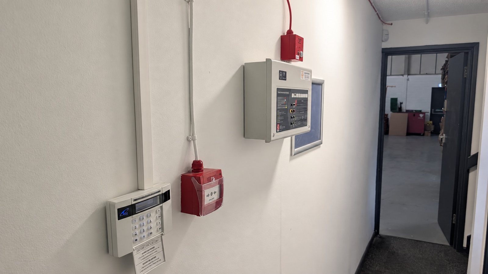 Corridor wall with an intruder alarm keypad, a fire alarm call point and a fire alarm control panel