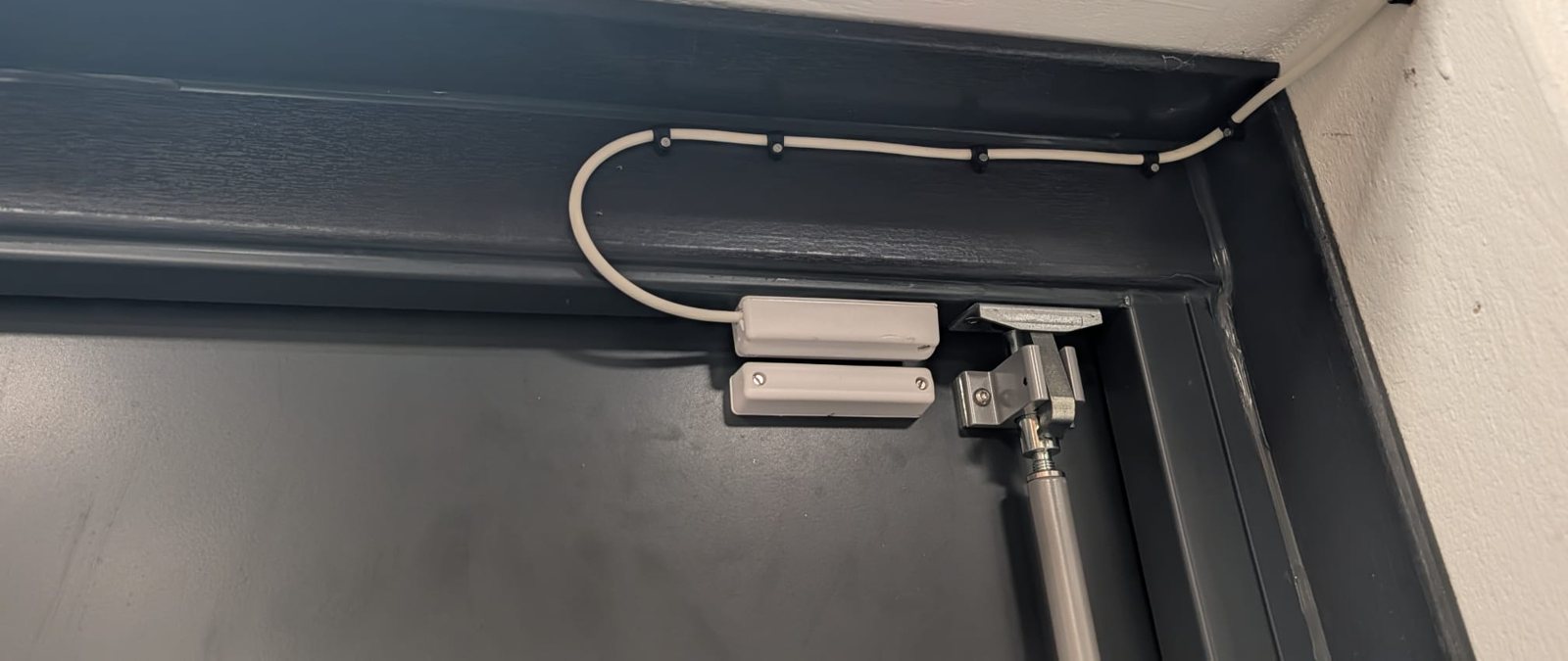 Surface-mounted magnetic door contact on a door frame, with clipped cable run