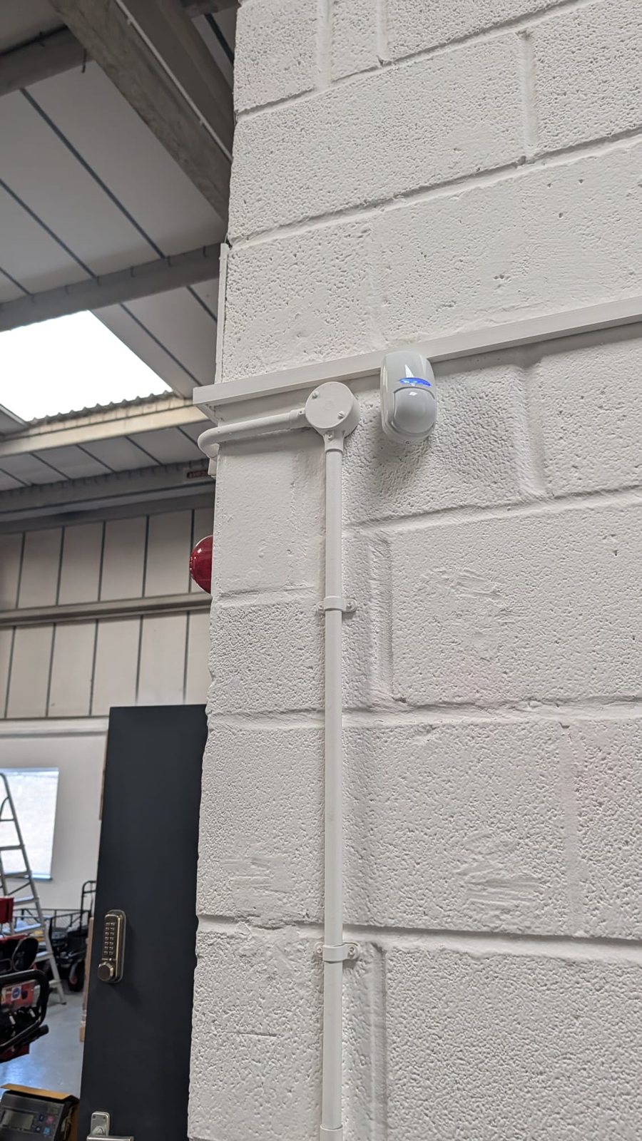 Intruder alarm motion detector above a neat white conduit run on a blockwork wall